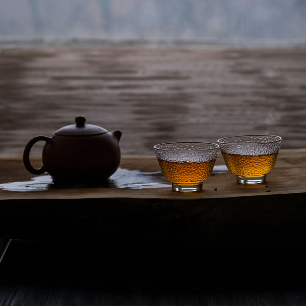 Tea set with a teapot and two cups on a wooden table with a blurred natural background